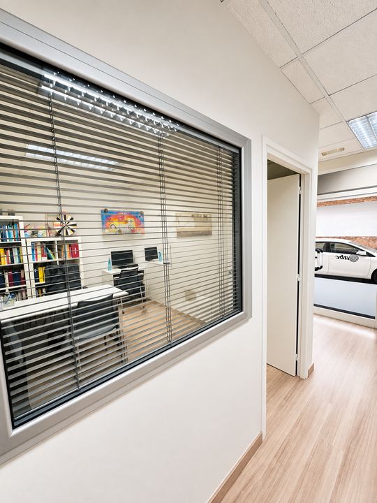 Finestra interior del passadís amb persianes que dona a una sala de consulta